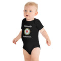 Blonde baby standing in a black short-sleeve infant bodysuit featuring the 'Distinctly Lutheran' text and a traditional colorful Luther Rose symbol. Cute Lutheran baby apparel and baptism gift ideas from Phoenix Anthem.