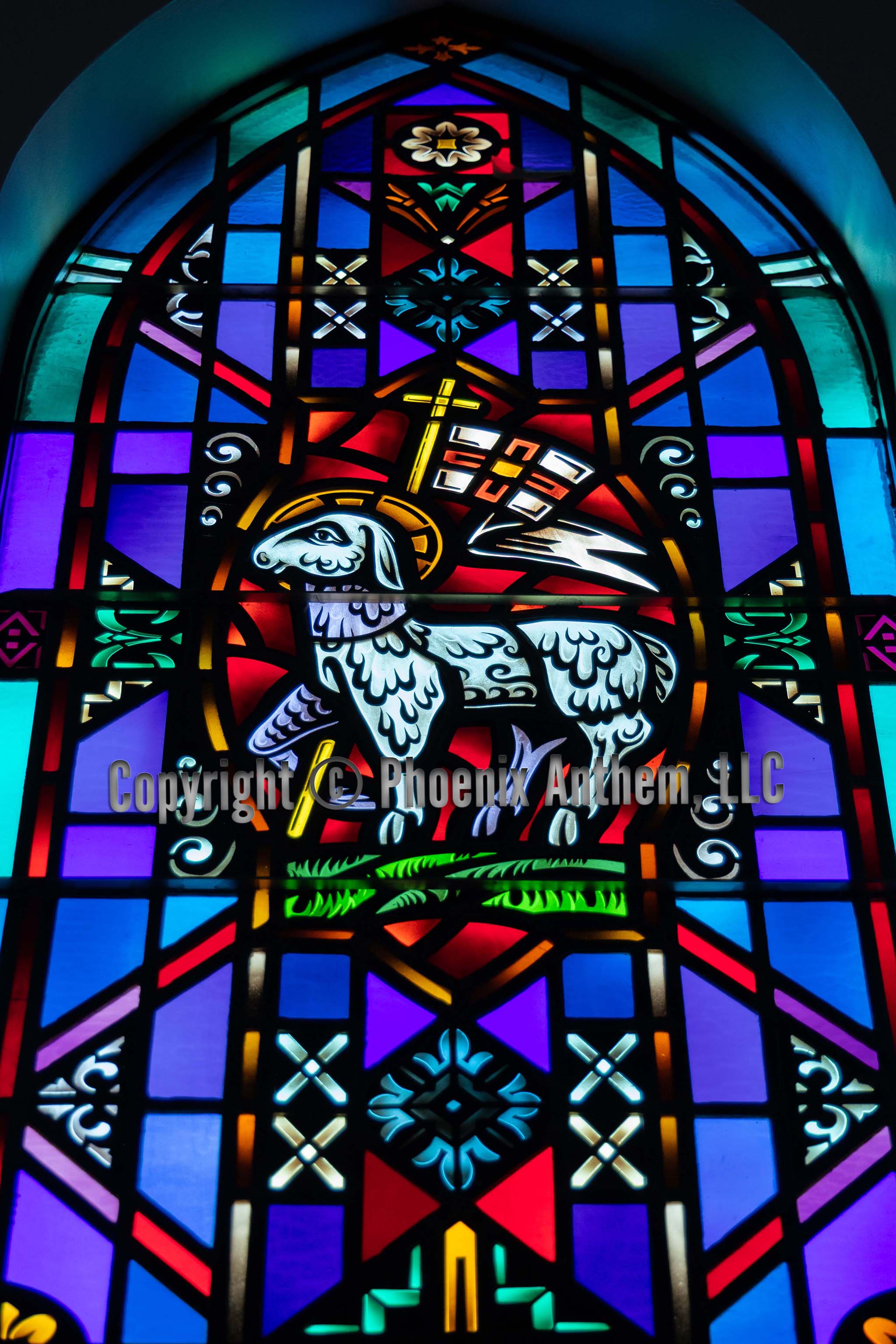 Stained glass window depicting the Lamb of God with a halo and victory banner surrounded by blue, red, and purple panels at Trinity Lutheran Church in Sheboygan, Wisconsin.