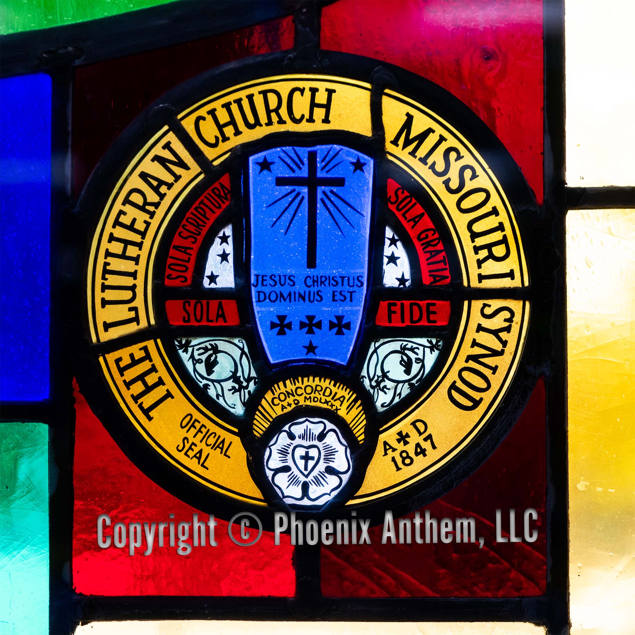 Stained glass window depicting the official seal of the Lutheran Church—Missouri Synod with a blue cross, red panels, and gold lettering at Trinity Lutheran Church in Sheboygan, Wisconsin.