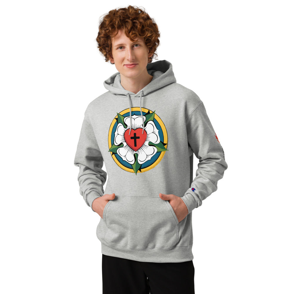 A young man with curly red hair smiling while wearing the light steel Champion Powerblend hoodie with the Luther Rose seal, styled as confessional Lutheran streetwear.
