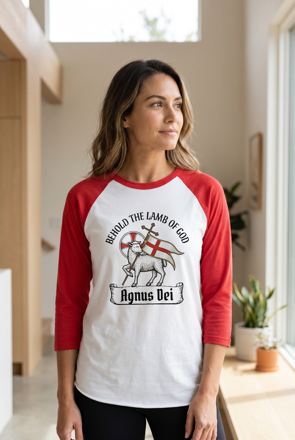 A woman looking to the side while wearing a white and red 3/4 sleeve Christian raglan shirt with a traditional 'Agnus Dei' Lamb of God illustration. Elegant liturgical faith-based apparel from Phoenix Anthem.
