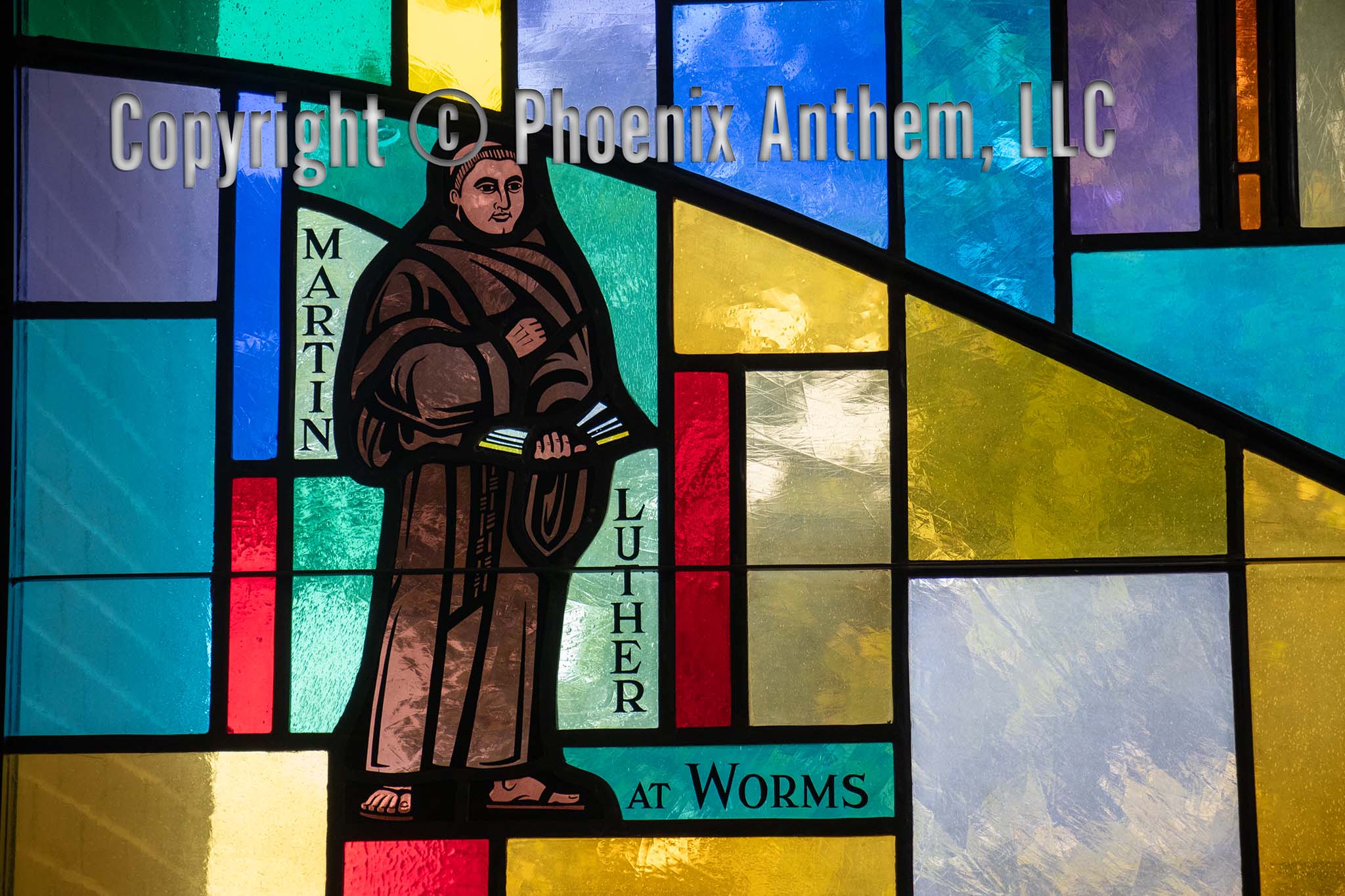Stained glass window depicting Martin Luther standing with an open book labeled ‘At Worms,’ surrounded by yellow, blue, and green glass panels at Trinity Lutheran Church in Sheboygan, Wisconsin.