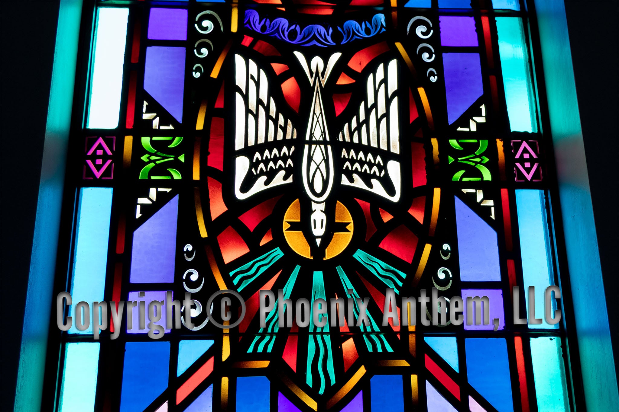 Stained glass window depicting the Holy Spirit as a descending dove with rays of blue and gold light surrounded by red and purple panels at Trinity Lutheran Church in Sheboygan, Wisconsin.