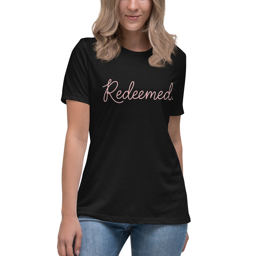A blonde woman wearing a black relaxed-fit Christian t-shirt featuring the word 'Redeemed.' in an elegant pink cursive font. Premium faith-based clothing for women from Phoenix Anthem.
