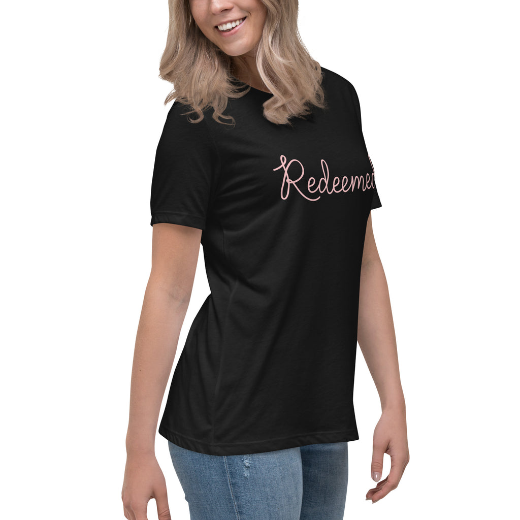 Three-quarter front right view of a blonde woman smiling and wearing a black relaxed-fit Christian t-shirt with the word 'Redeemed' in a pink cursive font. Casual faith-based fashion from Phoenix Anthem.