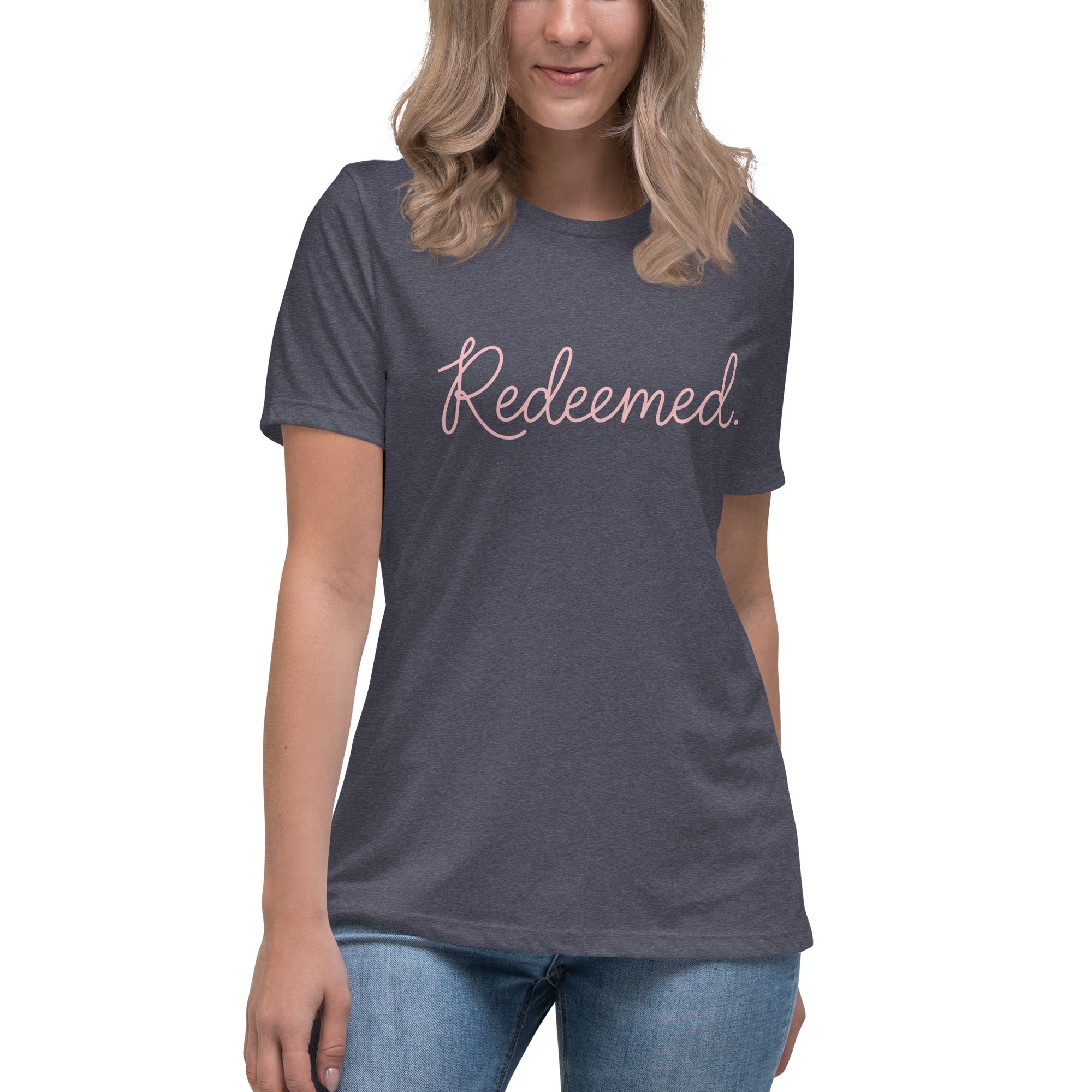 A blonde woman wearing a heather navy blue relaxed-fit Christian t-shirt featuring the word 'Redeemed.' in an elegant pink cursive font. Premium faith-based clothing for women from Phoenix Anthem.