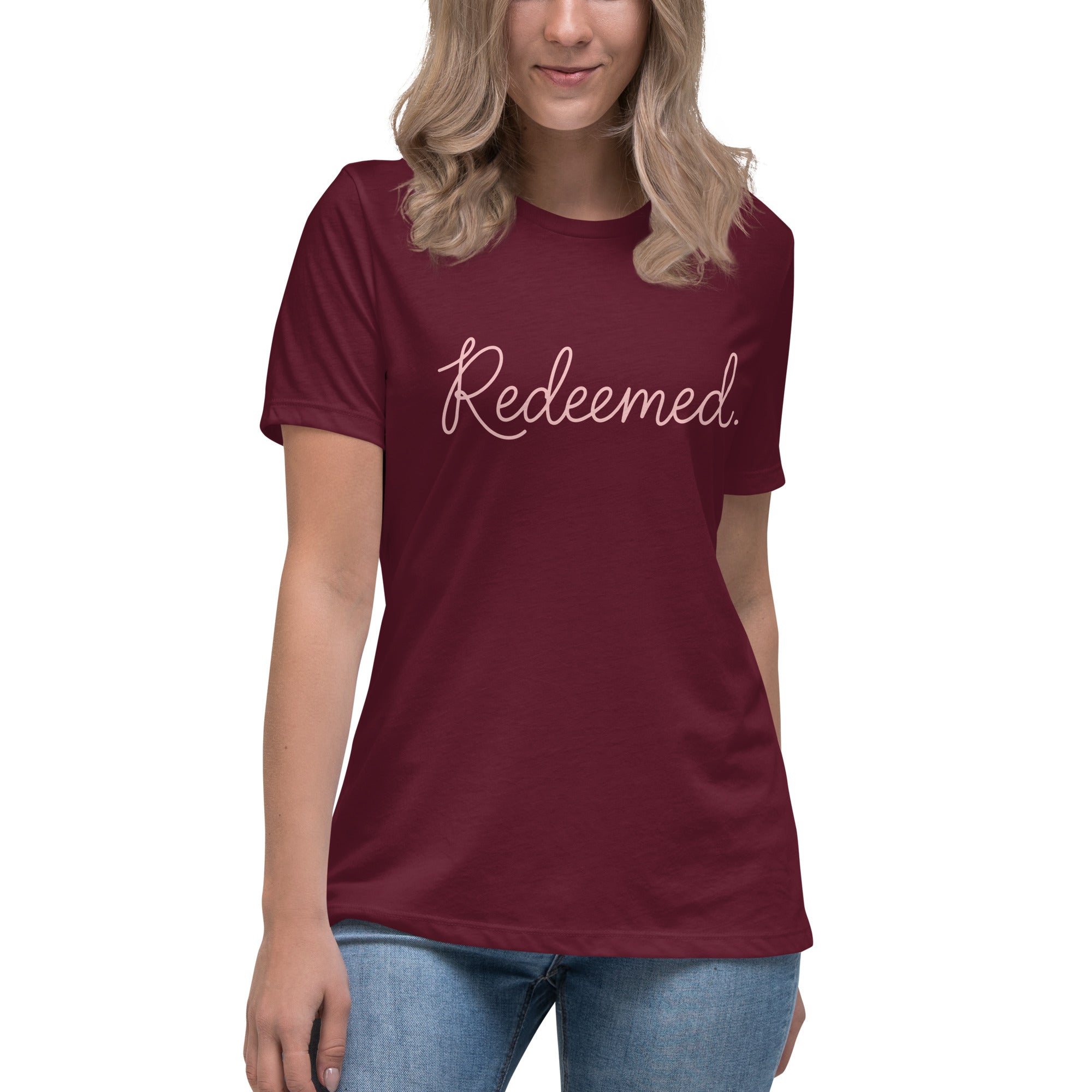 A blonde woman wearing a maroon relaxed-fit Christian t-shirt featuring the word 'Redeemed.' in an elegant pink cursive font. Premium faith-based clothing for women from Phoenix Anthem.