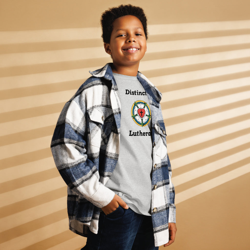 Smiling young boy wearing a plaid flannel over a sport grey children's Lutheran t-shirt displaying the 'Distinctly Lutheran' text and Luther Rose crest. Casual church apparel for kids.