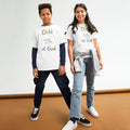 A young boy and girl standing side-by-side in a studio setting, wearing matching white classic youth t-shirts with a vibrant, colorful 'Child of God' graphic featuring a Holy Spirit dove. Coordinated faith-based children's apparel and Sunday school outfits from Phoenix Anthem.